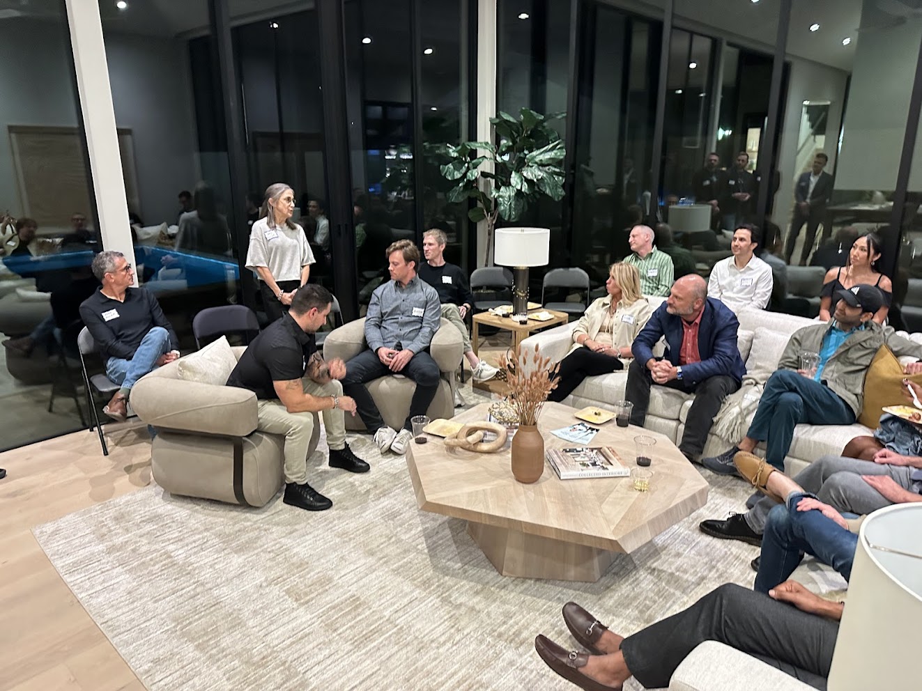 Approximately 15 to 20 accredited investors gathered in a luxury private home living room, listening to a speaker during an Astronomic Investor Dinner.